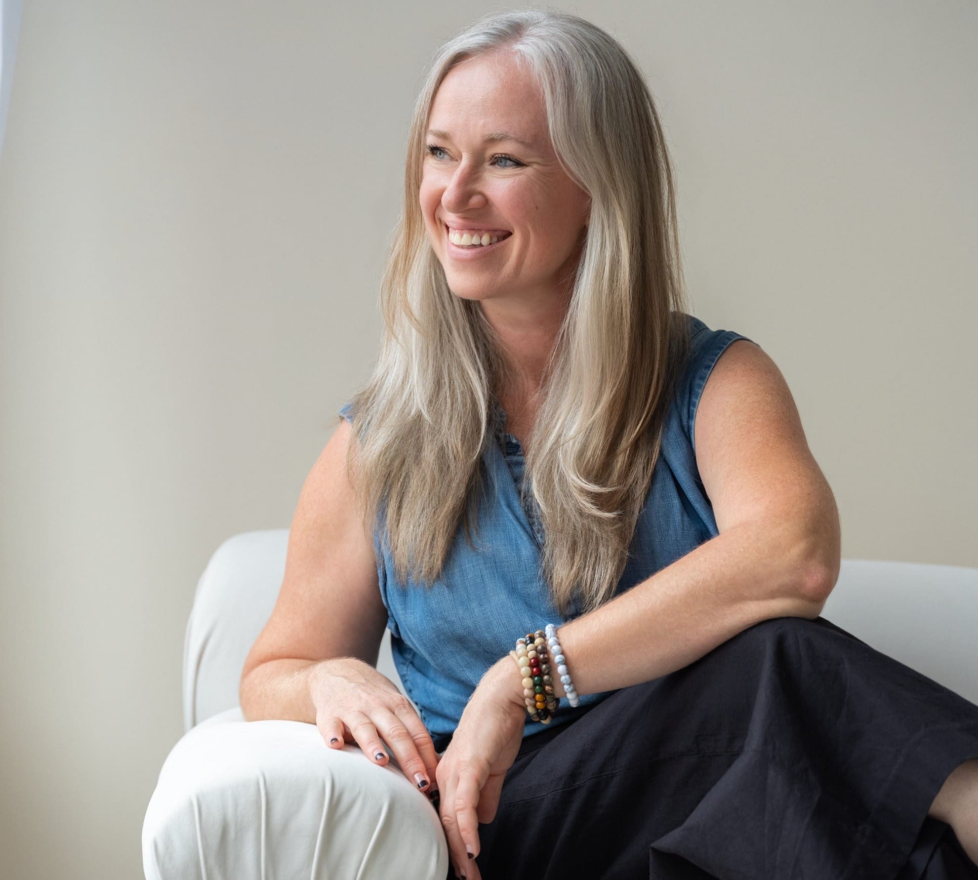 Silver-haired woman in a denim top laughing on a white sofa during a Louisville brand photography session